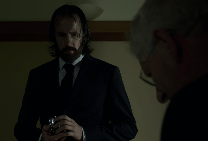 The Caretaker Eddie, stands in the office of Lockbridge School Owner holding an urn.